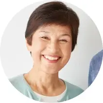 ホワイトのトップスに水色のカーディガンを着たショートカットで笑顔の70代女性の写真